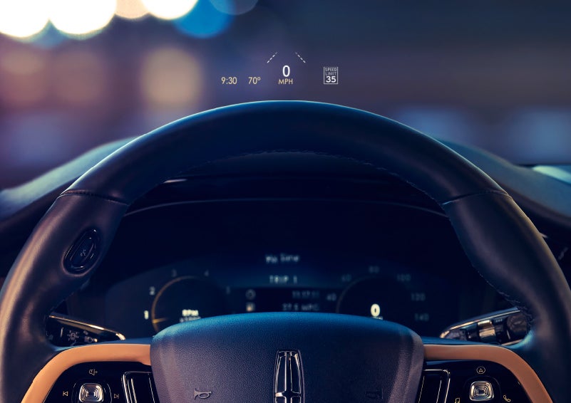 The available head-up display projects data on the windshield above the steering wheel inside a 2022 Lincoln Corsair as the driver navigates the city at night | Loveland Lincoln in Loveland CO
