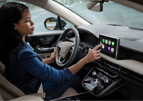 A woman in the driver’s seat of a 2022 Lincoln Corsair is touching the center digital screen to connect to Apple CarPlay<sup>®</sup> | Loveland Lincoln in Loveland CO