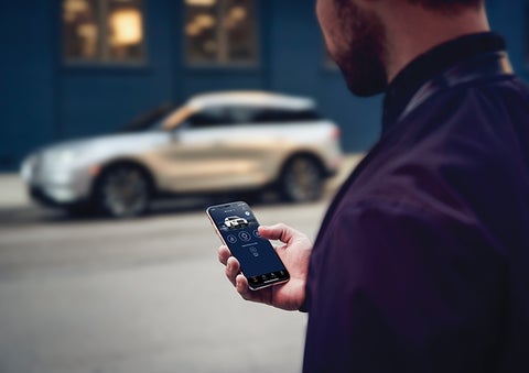 A person is shown interacting with a smartphone to connect to a Lincoln vehicle across the street. | Loveland Lincoln in Loveland CO