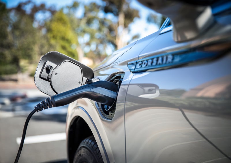A Lincoln electric charger is plugged into a 2022 Lincoln Corsair Grand Touring port as the body reflects the surroundings of a sun-soaked parking lot | Loveland Lincoln in Loveland CO