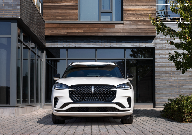 A white 2025 Lincoln Aviator® SUV is shown parked outside a modern building with gray brick and wood accents. | Loveland Lincoln in Loveland CO