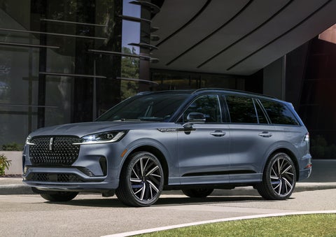 A gray 2025 Lincoln Aviator® SUV is parked outside a modern building showcasing the driver’s side of the vehicle. | Loveland Lincoln in Loveland CO