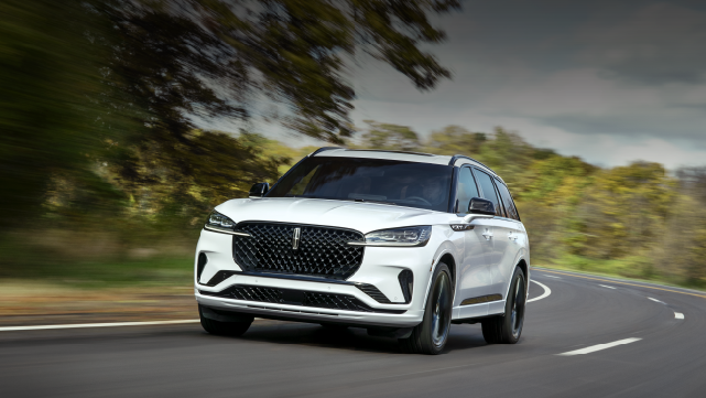 A white 2025 Lincoln Aviator® SUV is being driven down a road lined with trees. | Loveland Lincoln in Loveland CO