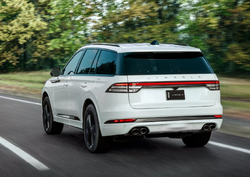 A white 2026 Lincoln Aviator® SUV is being driven away down a road lined with colorful trees. | Loveland Lincoln in Loveland CO