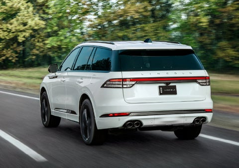 A white 2026 Lincoln Aviator® SUV is being driven away down a road lined with colorful trees. | Loveland Lincoln in Loveland CO