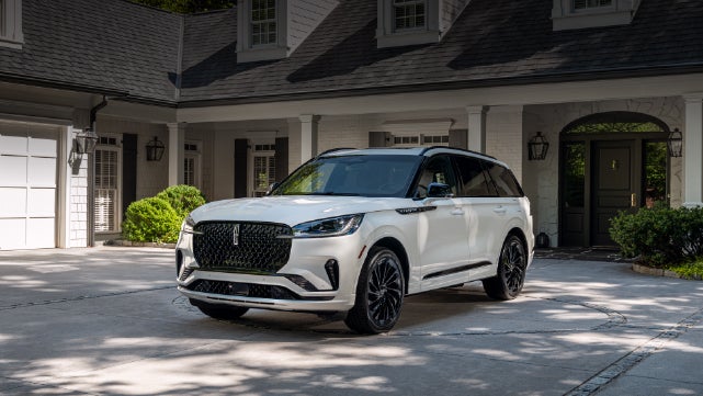 A white 2026 Lincoln Aviator® SUV is parked in the driveway of a luxury home. | Loveland Lincoln in Loveland CO