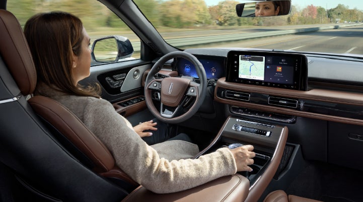 A 2027 Lincoln Aviator® SUV is being driven hands-free on a highway lined with trees. | Loveland Lincoln in Loveland CO