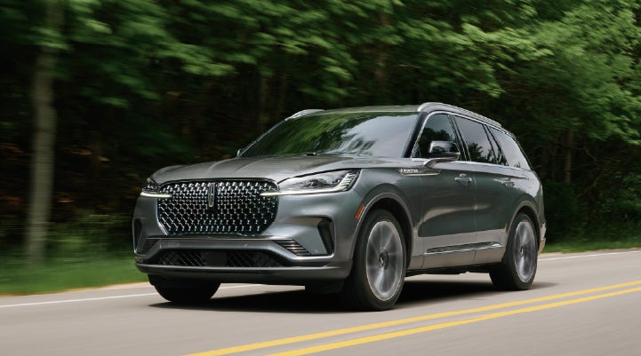 A 2027 Lincoln Aviator® SUV is being driven down a road lined with trees. | Loveland Lincoln in Loveland CO